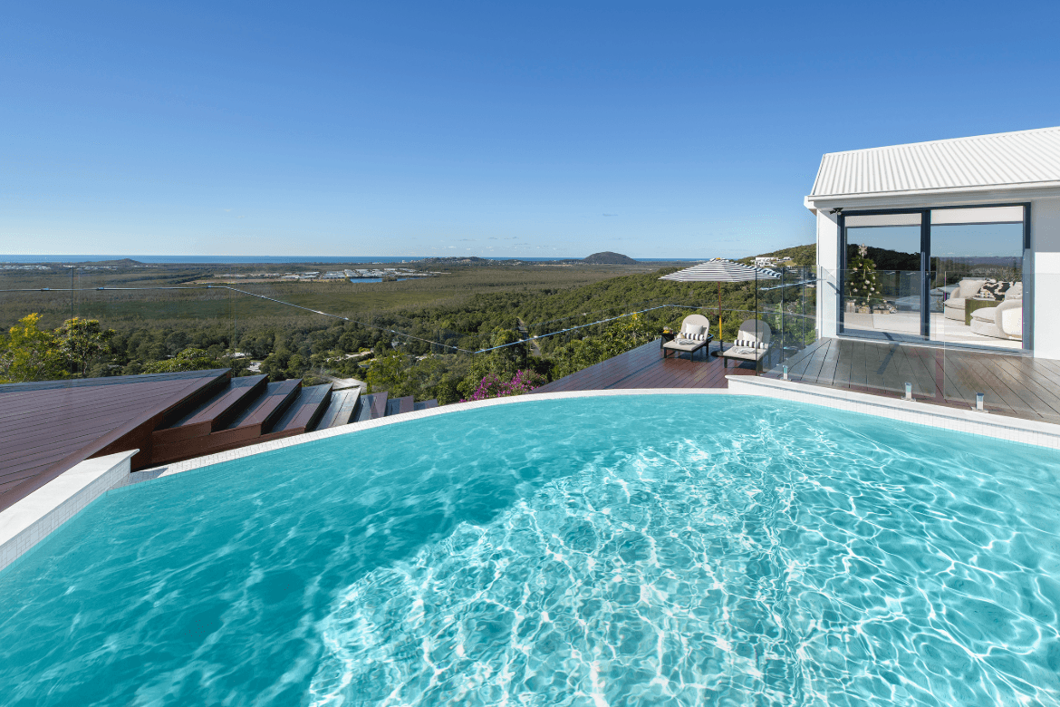 A stunning view of the ocean from the poolside of a sleek, modern home, showcasing blue waters and a clear sky.