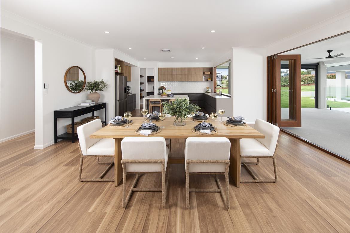 Dining room with a wooden table, white chairs, a green foliage centerpiece, and an open kitchen and patio view.