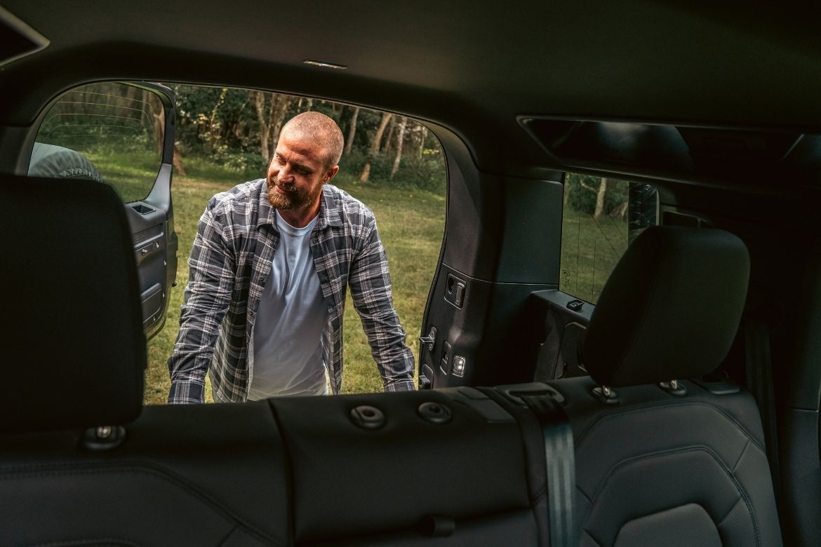 View from inside a V8 Land Rover Defender as a person stands at the open tailgate in a bushland setting