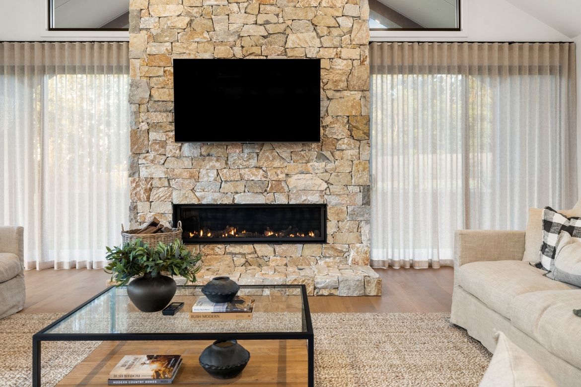 Elegant living room with a floor-to-ceiling natural stone fireplace, gas fire feature and light-filled interiors framed by sheer curtains