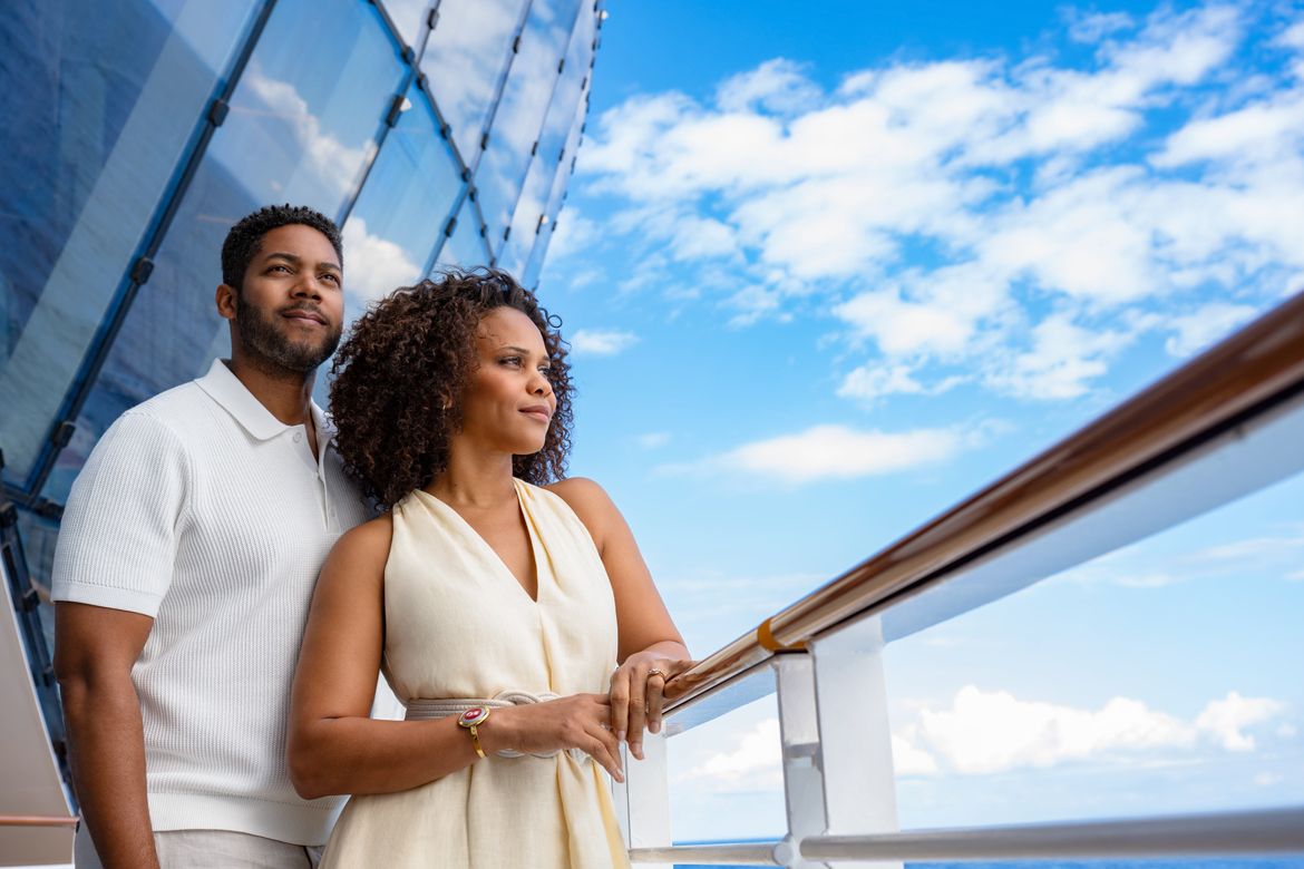 Couple standing together on a cruise ship deck and looking towards the horizon.