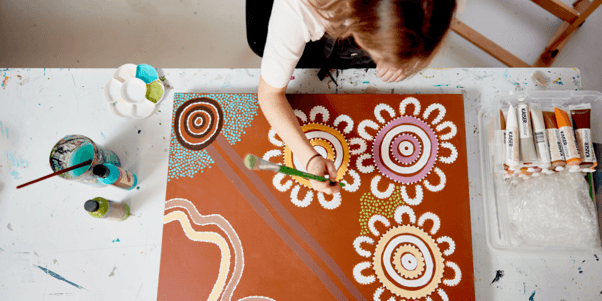 Overhead view of a QArt Studio artist painting an original artwork on canvas using colourful dot patterns and acrylic paints