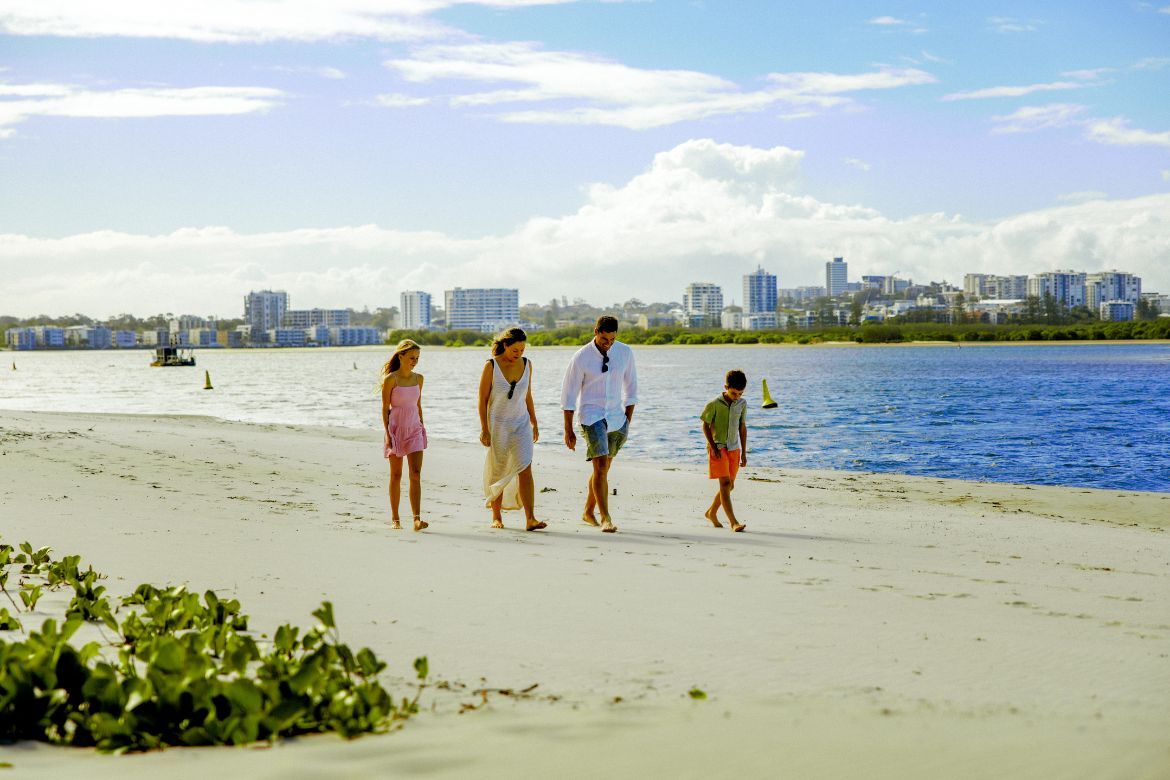 Family walking along the sandy shoreline of Golden Beach beside the calm waters of Pumicestone Passage.