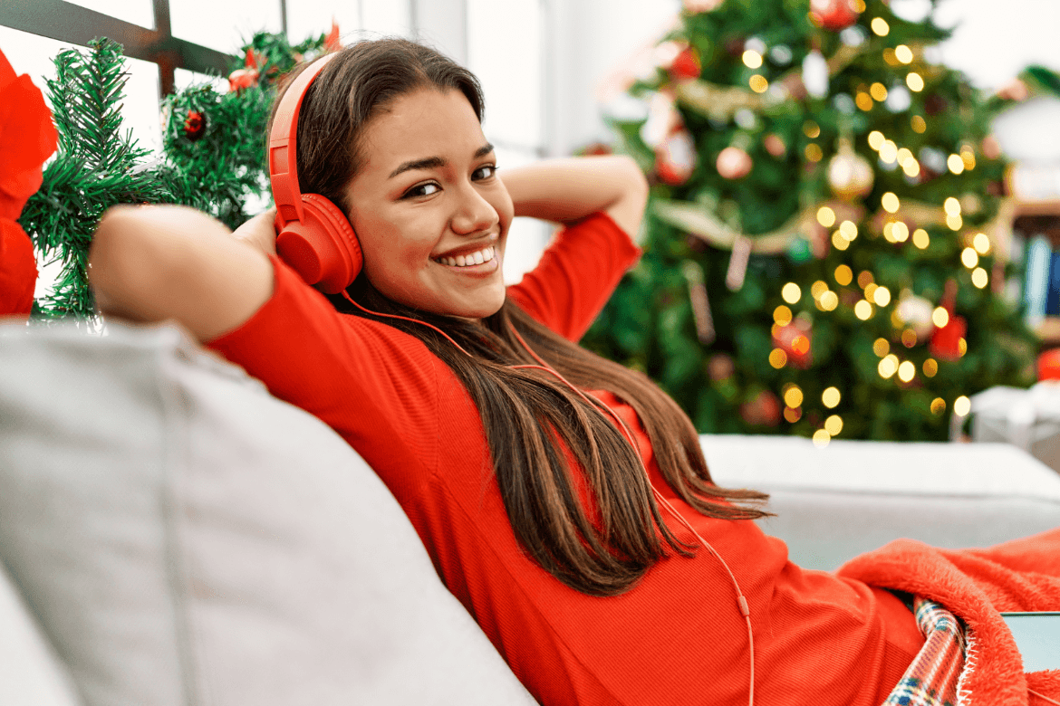 A woman in red sits comfortably on a couch, wearing headphones and enjoying her music