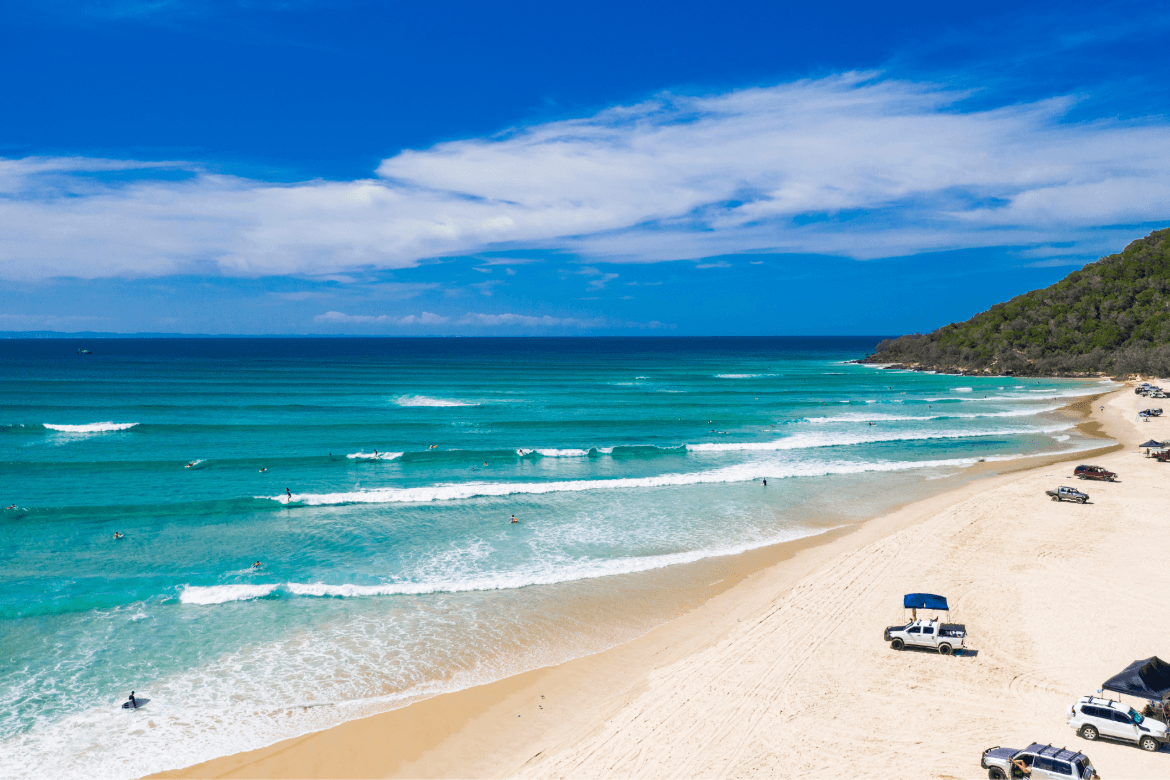 A sunny sandy beach with a few people enjoying the sun and surf, creating a relaxing seaside atmosphere.