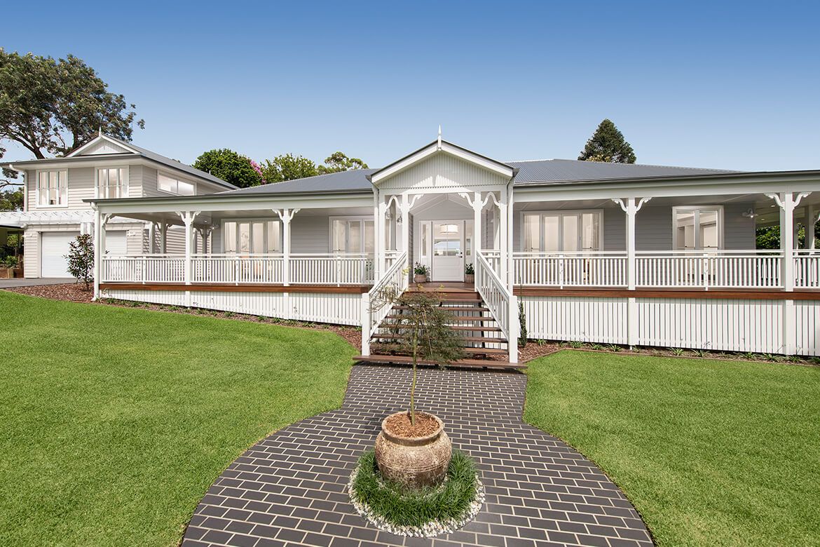 A large white house with a welcoming walkway leading up to the front door, surrounded by greenery