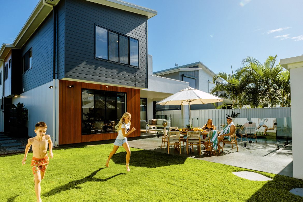 Children playing on the lawn while family relaxes in the outdoor entertaining area at Prize Home 469 in Golden Beach.
