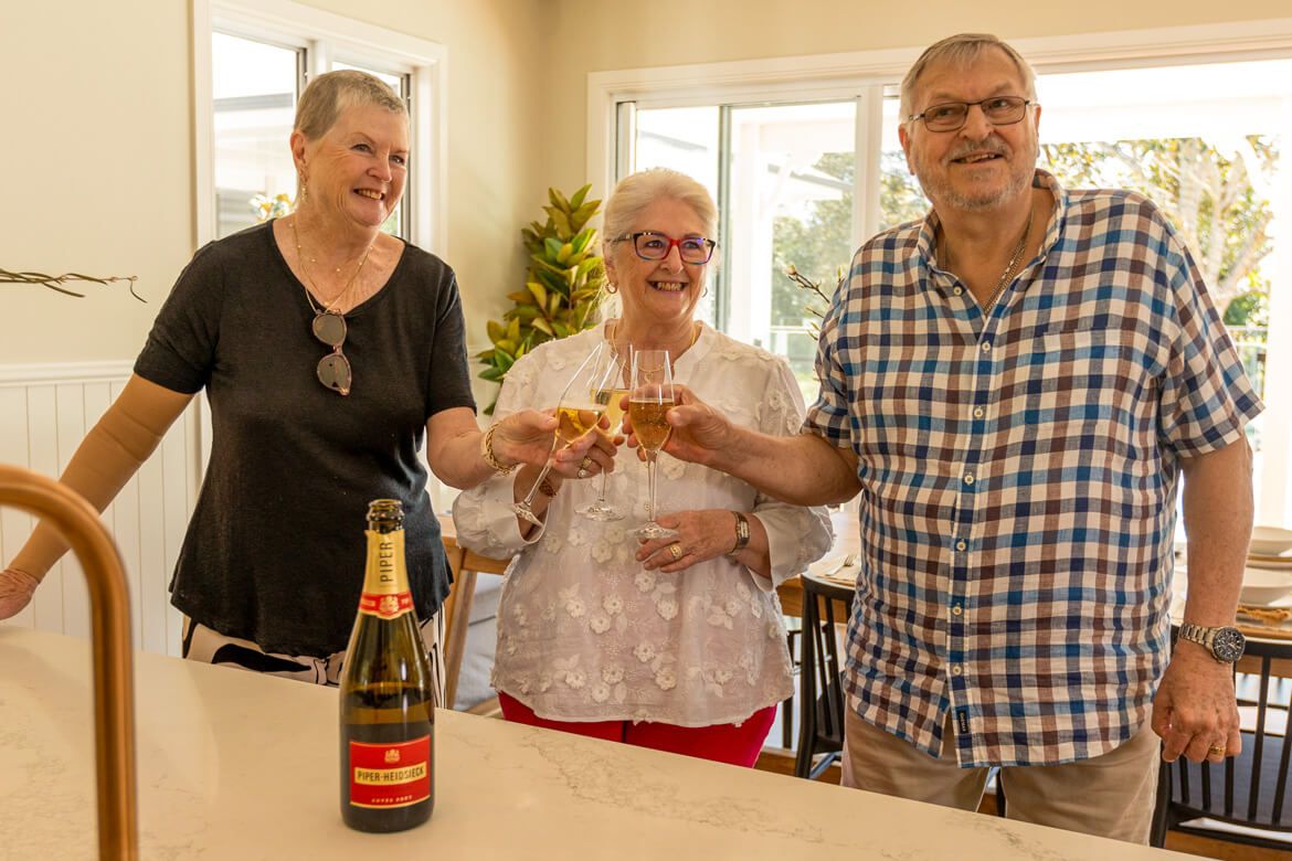 Three friends clink wine glasses together in a cozy kitchen, celebrating a special moment with laughter and joy.